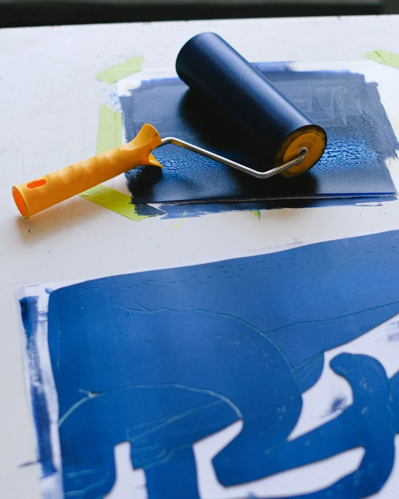 Rodillo entintado en azul apoyado sobre una prueba impresa en una sola tinta, con restos de color sobre la mesa de trabajo
