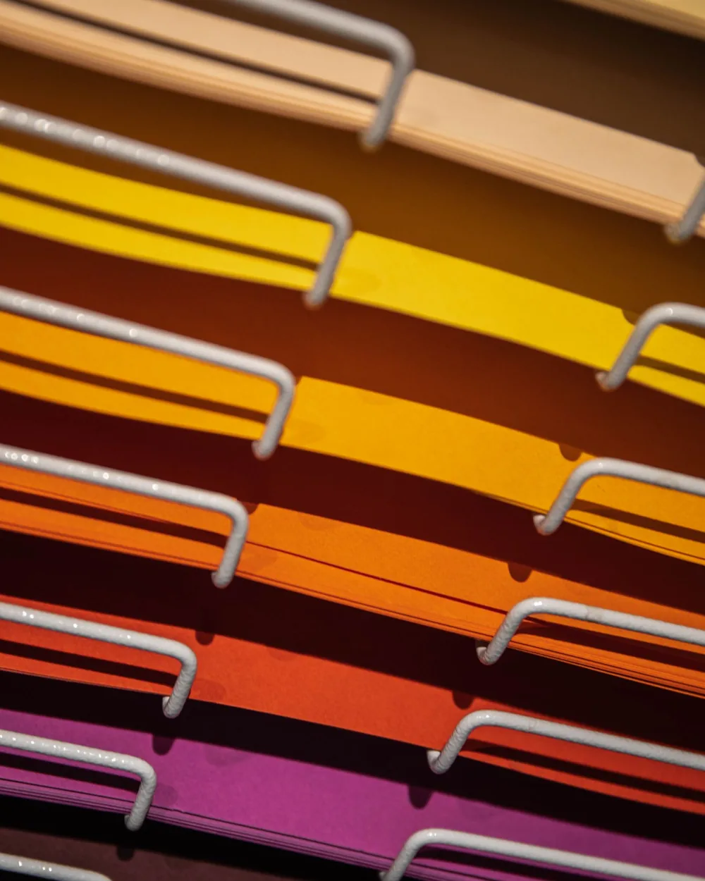Expositor con pliegos de papel de colores ordenados por tono, del crema al magenta, en un taller de impresión